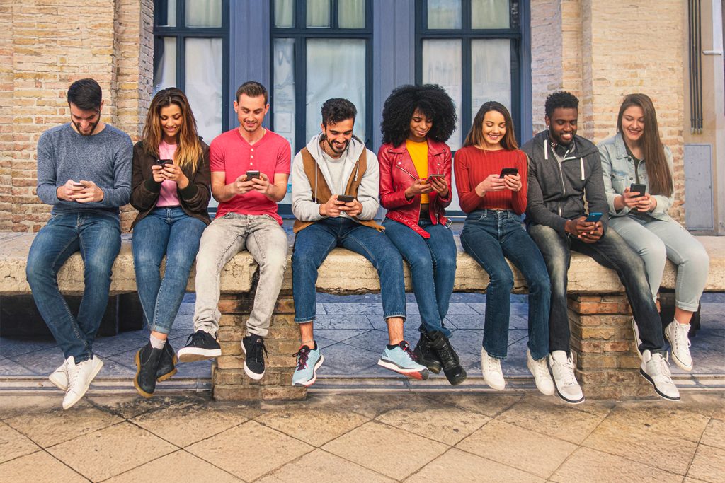 estudantes universitários sentados em um banco compartilhando fotos em seus smartphones